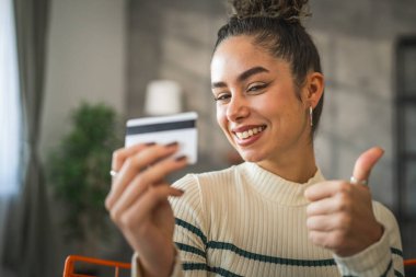 Yetişkin beyaz bir kadın mutlu bir şekilde gülümseyerek evde oturuyor banka kredi kartlarını online alışveriş konseptinde tutuyor gerçek insanlar uzay e-ticaretini kopyalıyor ya da rezervasyon yaptırıyor.