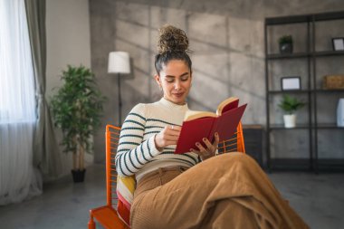 Genç bir yetişkin kadın. Bir kadın evde kitap okuyor ya da okuyor.