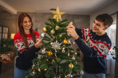 Genç çift Noel ağacını evde süslerle süslüyor.