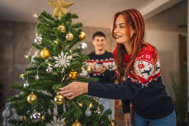 Genç bir kadın Noel ağacını evde süslerle süslüyor.