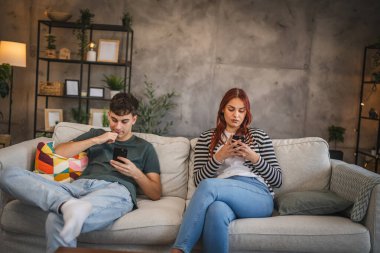 Genç çift koltuğa oturur ve cep telefonu kullanır. Telefon bağımlılığının gerçekçi bir fotoğrafı.