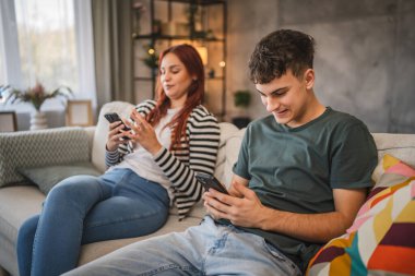 Genç çift koltuğa oturur ve cep telefonu kullanır. Telefon bağımlılığının gerçekçi bir fotoğrafı.