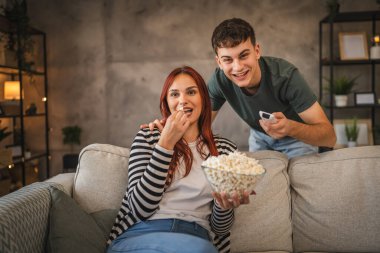 Genç çift film izler ve evde birlikte patlamış mısır yer.