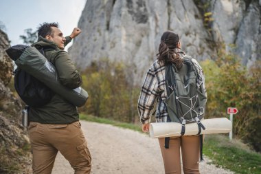 Bir çift erkek arkadaş ve kız arkadaş yürüyüşçüleri engebeli, doğal bir arazide pitoresk bir patika boyunca yürürler. Her ikisi de sırt çantaları ve açık hava teçhizatı ile donatılmıştır. Macera ve keşif sergilenmektedir.