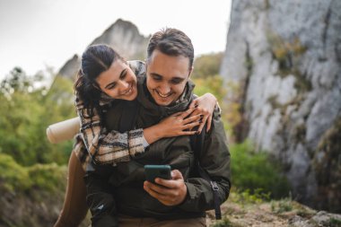 Kız arkadaş, erkek arkadaşı yürürken cep telefonunu kullanırken ona sarılıyor.