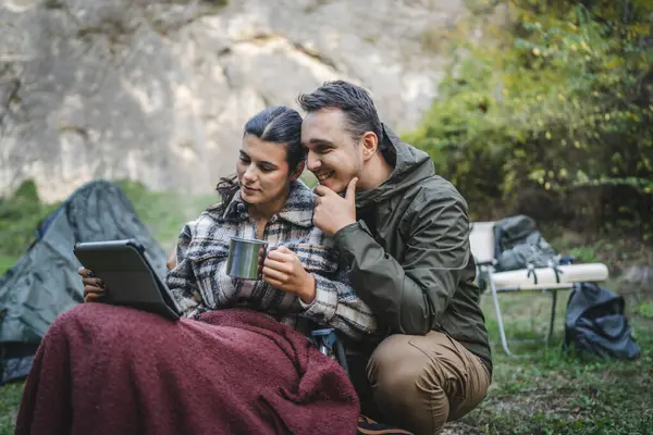 Mutlu çift kampçılar oturur ve çadırın önündeki dijital tablette film izlerler.