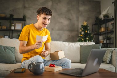 Genç yetişkin bir adam, laptop 'daki video görüşmesi sırasında tebrik kartını okur.