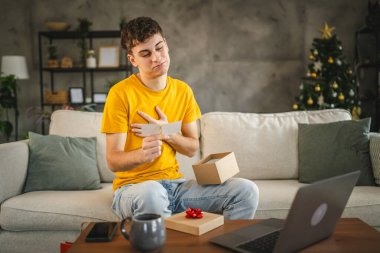 Genç yetişkin bir adam, laptop 'daki video görüşmesi sırasında tebrik kartını okur.