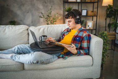 Kulaklıklı yetişkin bir adam laptoptan ders izler ve evden ders çalışır.