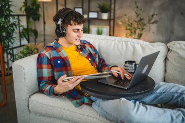 Kulaklıklı yetişkin bir adam laptoptan ders izler ve evden ders çalışır.