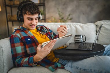 Kulaklıklı yetişkin bir adam laptoptan ders izler ve evden ders çalışır.