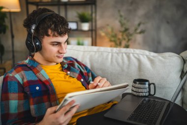 Kulaklıklı yetişkin bir adam laptoptan ders izler ve evden ders çalışır.