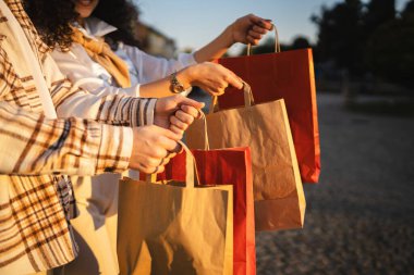 Genç yetişkin erkek ve kadınların elleri açık havada renkli alışveriş torbaları tutar.