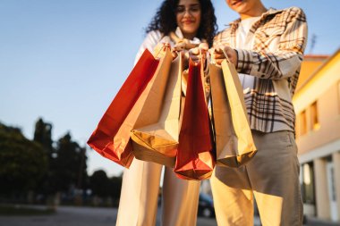 close up of young adult man and woman hands hold colorful shopping bags outdoor clipart