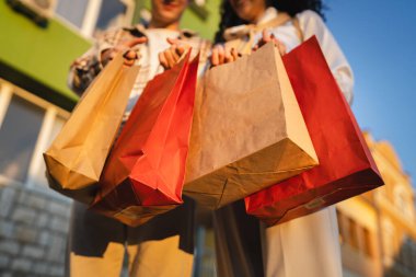 close up of young adult man and woman hands hold colorful shopping bags outdoor clipart