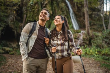Gezgin çiftler şelalenin etrafındaki ormanı yürüyüş çubuklarıyla keşfediyorlar.