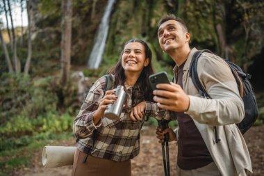 Yürüyüş yapan çiftler ormanı keşfederler, erkek arkadaşlar cep telefonlarını kullanırken kız arkadaşlar metal şişeden içerler.