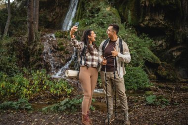 Yürüyüş yapan çift, şelalenin önünde kendi portresini ya da görüntüsünü çeker.