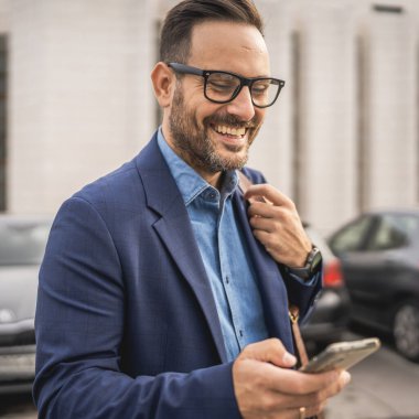 Yetişkin gülüşlü işadamı park yerinde durup cep telefonu kullanıyor.