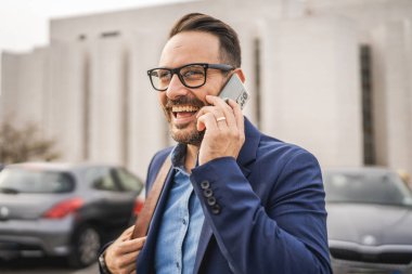 Yetişkin, neşeli iş adamı park yerinde, ön şirkette duruyor ve cep telefonuyla konuşuyor.