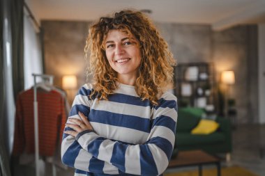 Evde kıvırcık saçlı, mutlu gülümseyen yetişkin beyaz kadın portresi.