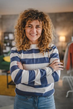 Evde kıvırcık saçlı, mutlu gülümseyen yetişkin beyaz kadın portresi.