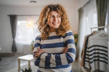 Evde kıvırcık saçlı, mutlu gülümseyen yetişkin beyaz kadın portresi.