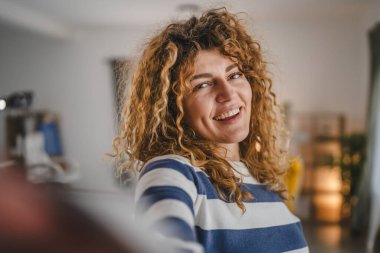 Evde kıvırcık saçlı, yetişkin beyaz bir kadının portresi. Mutlu bir gülümseme. Kendi portresi çirkin kullanıcı tarafından oluşturulmuş.