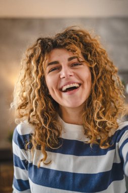 Evde kıvırcık saçlı, yetişkin beyaz bir kadının portresi. Mutlu bir gülümseme. Kendi portresi çirkin kullanıcı tarafından oluşturulmuş.