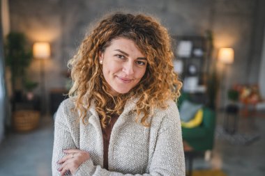 Evde kıvırcık saçlı, mutlu gülümseyen yetişkin beyaz kadın portresi.