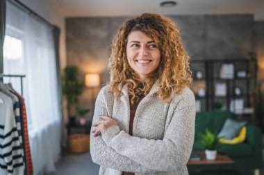 Evde kıvırcık saçlı, mutlu gülümseyen yetişkin beyaz kadın portresi.