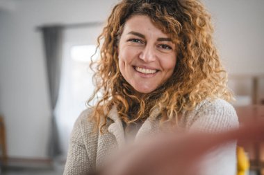 Evde kıvırcık saçlı, yetişkin beyaz bir kadının portresi. Mutlu bir gülümseme. Kendi portresi çirkin kullanıcı tarafından oluşturulmuş.