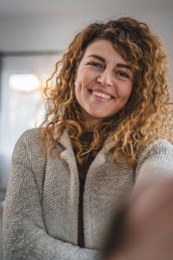 Evde kıvırcık saçlı, yetişkin beyaz bir kadının portresi. Mutlu bir gülümseme. Kendi portresi çirkin kullanıcı tarafından oluşturulmuş.