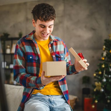 Genç yetişkin bir adam Noel hediyesini evde açıyor.