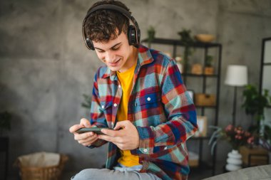 Kulaklıklı yetişkin bir genç cep telefonuyla video oyunu oynuyor.