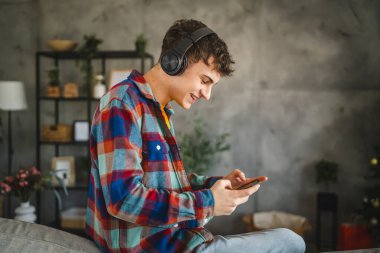 Kulaklıklı yetişkin bir genç cep telefonuyla video oyunu oynuyor.