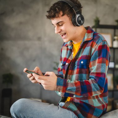 Kulaklıklı yetişkin bir genç cep telefonuyla video oyunu oynuyor.