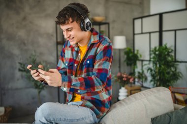 Kulaklıklı yetişkin bir genç cep telefonuyla video oyunu oynuyor.
