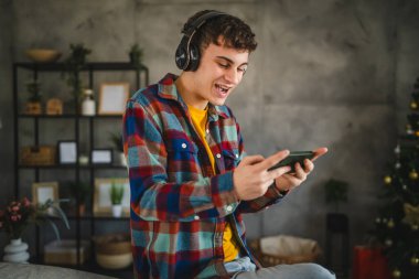 Kulaklıklı yetişkin bir genç cep telefonuyla video oyunu oynuyor.