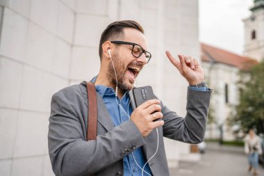 İş adamı kulaklıkla ve cep telefonuyla müzik dinliyor ve eğleniyor