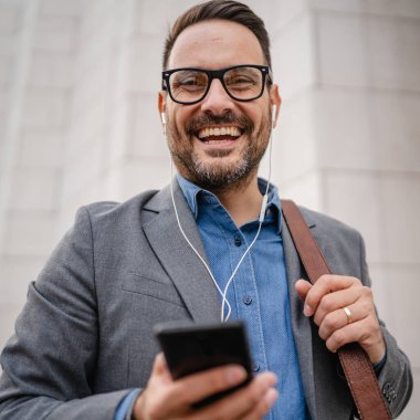 İş adamı kulaklıkla müzik dinler ve cep telefonu kullanır.