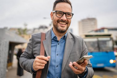 Yetişkin işadamı otobüs durağında cep telefonu kullanıyor