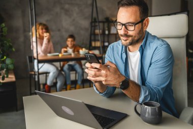Baba evde çalışırken arka planda ailesini gezdirirken cep telefonu kullanıyor.