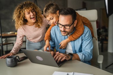 Baba, ailesi onun dikkatini dağıtırken ve oğlu da onu kollarken evden çalışmaya çalışıyor.