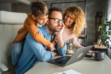 Baba, ailesi onun dikkatini dağıtırken ve oğlu da onu kollarken evden çalışmaya çalışıyor.