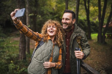 Karı koca yürüyüşçüleri sırt çantasıyla gezerler. Ormanda yürüyüş yaparken kendi portresini ya da video görüntülerini çekerler.