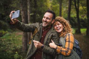 Karı koca yürüyüşçüleri sırt çantasıyla gezerler. Ormanda yürüyüş yaparken kendi portresini ya da video görüntülerini çekerler.