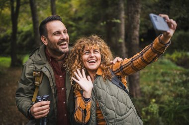 Karı koca yürüyüşçüleri sırt çantasıyla gezerler. Ormanda yürüyüş yaparken kendi portresini ya da video görüntülerini çekerler.