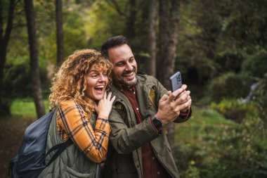 Karı koca yürüyüşçüleri sırt çantasıyla gezerler. Ormanda yürüyüş yaparken kendi portresini ya da video görüntülerini çekerler.