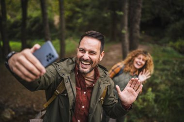 Yetişkin adam yürüyüşçüsü karısı arkasında dururken kendi fotoğrafını çeker.
